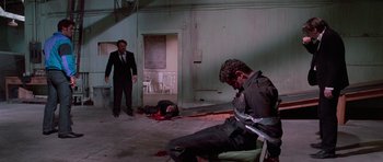Movie still from “Reservoir Dogs” (1992), directed by Quentin Tarantino – A man in a suit and tie sitting in front of another man in a suit and tie; Wide shot, Over the shoulder angle
