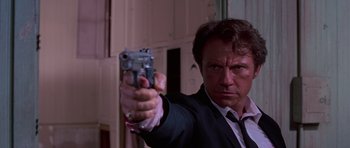 Movie still from “Reservoir Dogs” (1992), directed by Quentin Tarantino – A man in a suit and tie holding a gun in his hand; Close Up shot, Low angle