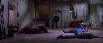 Movie still from “Reservoir Dogs” (1992), directed by Quentin Tarantino – A man in a suit standing in front of some corpses in a room; Wide shot, High angle