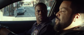 Movie still from “Ride Along” (2014), directed by Tim Story – A cop sitting in the back seat of a car; Close Up shot, Over the shoulder angle