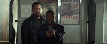 Movie still from “Ride Along” (2014), directed by Tim Story – Two men standing next to each other holding guns; Medium shot, Over the shoulder angle