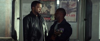 Movie still from “Ride Along” (2014), directed by Tim Story – Two men in leather jackets talking to each other in a room; Medium shot, Over the shoulder angle