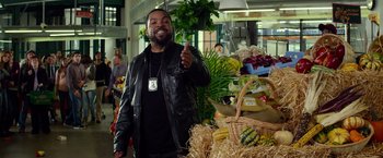 Movie still from “Ride Along” (2014), directed by Tim Story – A man standing in front of a display of vegetables; Medium shot, Over the shoulder angle