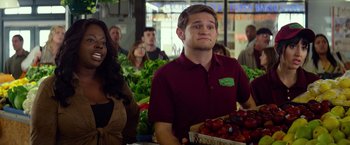 Movie still from “Ride Along” (2014), directed by Tim Story – A man holding a basket of fruit in front of a group of people; Medium shot, Over the shoulder angle