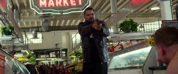 Movie still from “Ride Along” (2014), directed by Tim Story – A man holding a gun while standing in front of a market; Wide shot, Over the shoulder angle