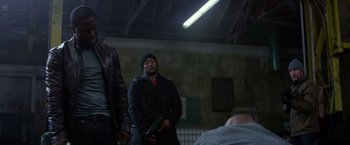 Movie still from “Ride Along” (2014), directed by Tim Story – A man holding a gun while standing next to another man; Medium shot, Over the shoulder angle
