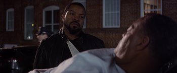 Movie still from “Ride Along” (2014), directed by Tim Story – A man standing next to another man in front of a brick building; Close Up shot, Over the shoulder angle