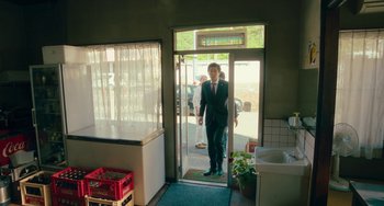 Movie still from “Ride or Die” (2021), directed by Ryûichi Hiroki – A man in a suit is standing in the doorway of a store; Wide shot, Low angle