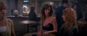 Movie still from “Road House” (1989), directed by Rowdy Herrington – A woman sitting at a table with a glass of wine; Medium shot, Over the shoulder angle