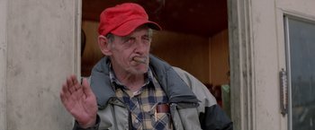 Movie still from “Road House” (1989), directed by Rowdy Herrington – An older man wearing a red hat smoking a cigarette; Medium shot, Low angle