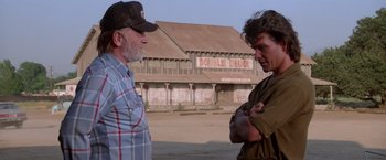 Movie still from “Road House” (1989), directed by Rowdy Herrington – Two men standing next to each other in front of an old building; Medium shot, Over the shoulder angle