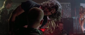 Movie still from “Road House” (1989), directed by Rowdy Herrington – A man with long dark hair is talking to another man in a dark room; Close Up shot, Over the shoulder angle