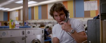 Movie still from “Road House” (1989), directed by Rowdy Herrington – A man holding a phone up to his ear in front of a washing machine; Close Up shot, Low angle
