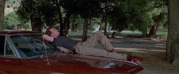 Movie still from “Road House” (1989), directed by Rowdy Herrington – A man laying on the hood of a car in a wooded area; Wide shot, Low angle