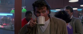 Movie still from “Road House” (1989), directed by Rowdy Herrington – A man drinking from a white mug while wearing a robe; Medium shot, Low angle