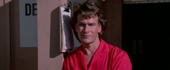 Movie still from “Road House” (1989), directed by Rowdy Herrington – A man in a red shirt is holding a clipboard; Close Up shot, Low angle