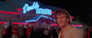 Movie still from “Road House” (1989), directed by Rowdy Herrington – A man standing in front of a group of people; Close Up shot, Low angle