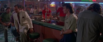 Movie still from “Road House” (1989), directed by Rowdy Herrington – A group of people standing around a bar with drinks; Medium shot, Over the shoulder angle