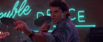 Movie still from “Road House” (1989), directed by Rowdy Herrington – A man holding a cymbal in front of a neon sign; Close Up shot, Low angle