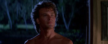 Movie still from “Road House” (1989), directed by Rowdy Herrington – A shirtless man with long curly hair looks at the camera; Close Up shot, Low angle