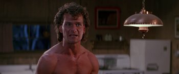 Movie still from “Road House” (1989), directed by Rowdy Herrington – A shirtless man with long brown hair in a living room; Close Up shot, Low angle