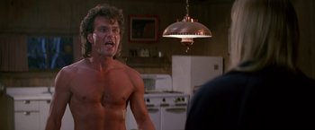 Movie still from “Road House” (1989), directed by Rowdy Herrington – A shirtless man standing in front of an oven in a kitchen; Medium shot, Low angle