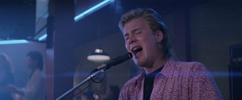 Movie still from “Road House” (1989), directed by Rowdy Herrington – A young man singing into a microphone in front of a crowd; Close Up shot, Low angle