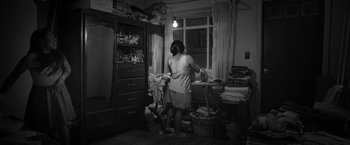 Movie still from “Roma” (2018), directed by Alfonso Cuarón – A woman is standing in a room with a bunch of clothes; Wide shot, High angle