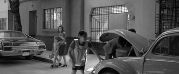 Movie still from “Roma” (2018), directed by Alfonso Cuarón – A group of people standing next to a car with an open hood; Wide shot, High angle