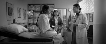 Movie still from “Roma” (2018), directed by Alfonso Cuarón – A woman sitting on a table talking to two other women; Medium shot, Low angle