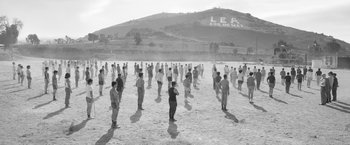 Movie still from “Roma” (2018), directed by Alfonso Cuarón – A black and white photo of people standing in the sand; Extreme Wide shot, High angle