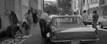 Movie still from “Roma” (2018), directed by Alfonso Cuarón – A man standing on the side of the road next to a parked car; Wide shot, High angle