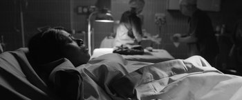 Movie still from “Roma” (2018), directed by Alfonso Cuarón – A patient lying in a hospital bed while a nurse stands in the background; Medium shot, Over the shoulder angle