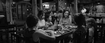 Movie still from “Roma” (2018), directed by Alfonso Cuarón – A group of people sitting at a table with food; Medium shot, Over the shoulder angle