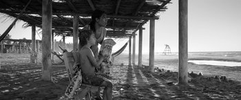 Movie still from “Roma” (2018), directed by Alfonso Cuarón – A woman and a child sitting on a beach; Medium shot, Low angle