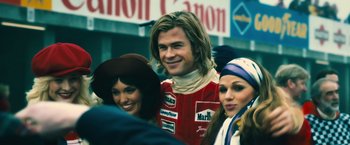 Movie still from “Rush” (2013), directed by Ron Howard – A man and two women are posing for a picture; Medium shot, Low angle