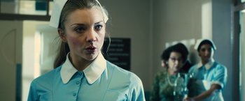Movie still from “Rush” (2013), directed by Ron Howard – A woman in a blue shirt is standing in front of another woman; Close Up shot, Over the shoulder angle