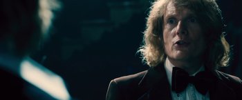 Movie still from “Rush” (2013), directed by Ron Howard – A man with long blonde curly hair wearing a suit; Close Up shot, Over the shoulder angle