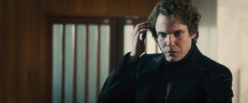 Movie still from “Rush” (2013), directed by Ron Howard – A man in a black suit is holding his hand to his head; Close Up shot, Over the shoulder angle