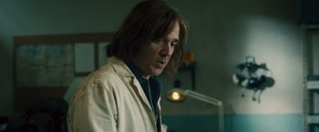 Movie still from “Rush” (2013), directed by Ron Howard – A man in a lab coat standing next to a light fixture; Medium shot, Low angle