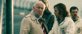 Movie still from “Rush” (2013), directed by Ron Howard – An older man in a trench coat and a tie; Close Up shot, Over the shoulder angle