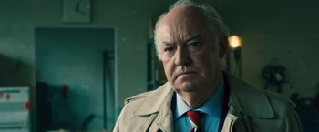 Movie still from “Rush” (2013), directed by Ron Howard – An older man wearing a trench coat and a tie; Close Up shot, Low angle