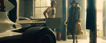 Movie still from “Rush” (2013), directed by Ron Howard – A man and a woman standing next to each other in a garage; Wide shot, Low angle