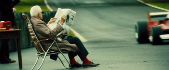 Movie still from “Rush” (2013), directed by Ron Howard – A man sitting in a chair reading a newspaper; Wide shot, Low angle