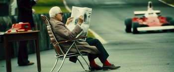 Movie still from “Rush” (2013), directed by Ron Howard – An older man sitting in a chair reading a newspaper; Medium shot, High angle