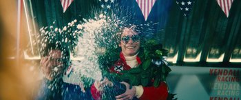 Movie still from “Rush” (2013), directed by Ron Howard – A man in a red suit is splashing a plant; Medium shot, Overhead angle