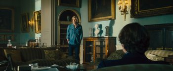 Movie still from “Rush” (2013), directed by Ron Howard – A man standing in a living room next to a table; Medium shot, Over the shoulder angle