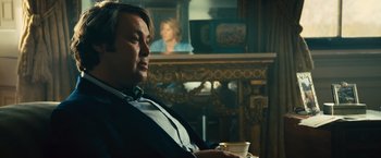 Movie still from “Rush” (2013), directed by Ron Howard – A man sitting in front of a fireplace holding a coffee cup; Medium shot, Over the shoulder angle