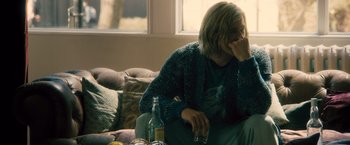 Movie still from “Rush” (2013), directed by Ron Howard – A woman sitting on a couch with a bottle of alcohol; Medium shot, Over the shoulder angle