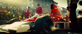 Movie still from “Rush” (2013), directed by Ron Howard – A man in a red racing suit sitting in a red race car; Wide shot, Low angle